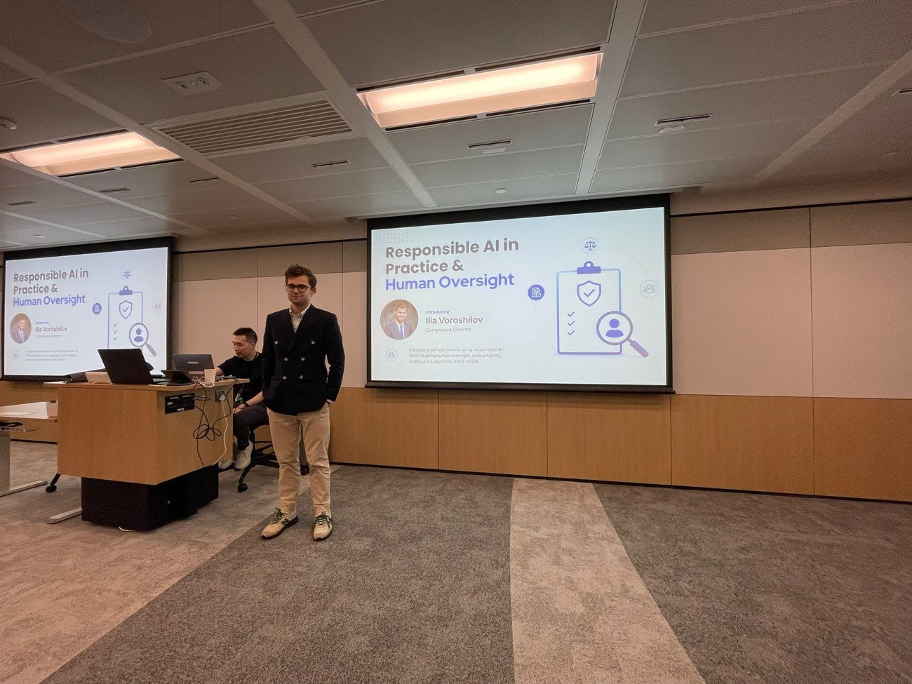 A presenter stands beside a projected slide titled Responsible AI in Practice and Human Oversight in a meeting room.